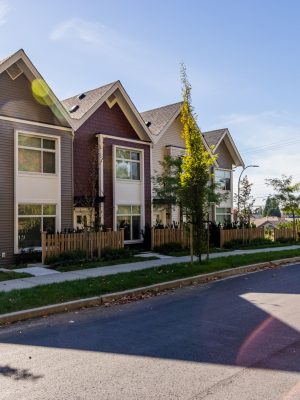 Row of modern townhouses with picket fences in Mission, BC, Canada, under a clear blue sky. The scene captures a tranquil suburban setting on a bright sunny day.